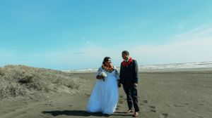 Bride and groom walking hand in hand on a black sand beach under a blue sky.