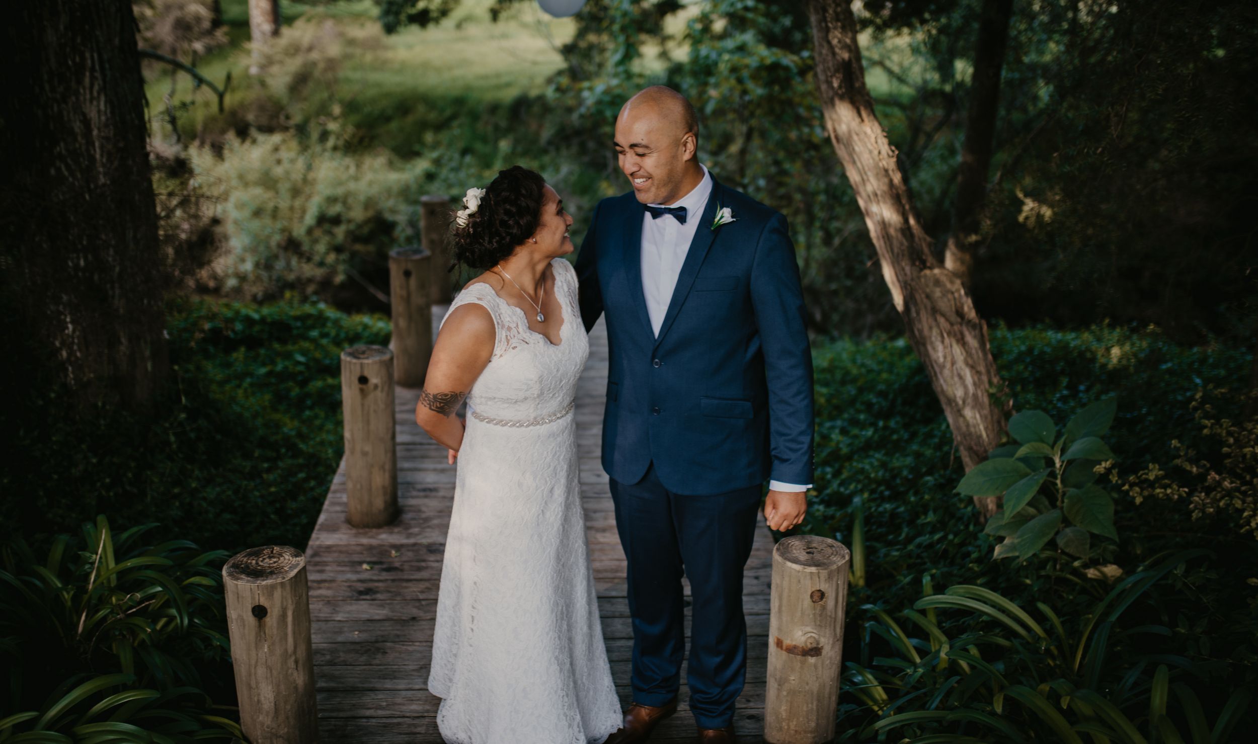 Bride in white dress and groom in navy suit share a tender look in garden.