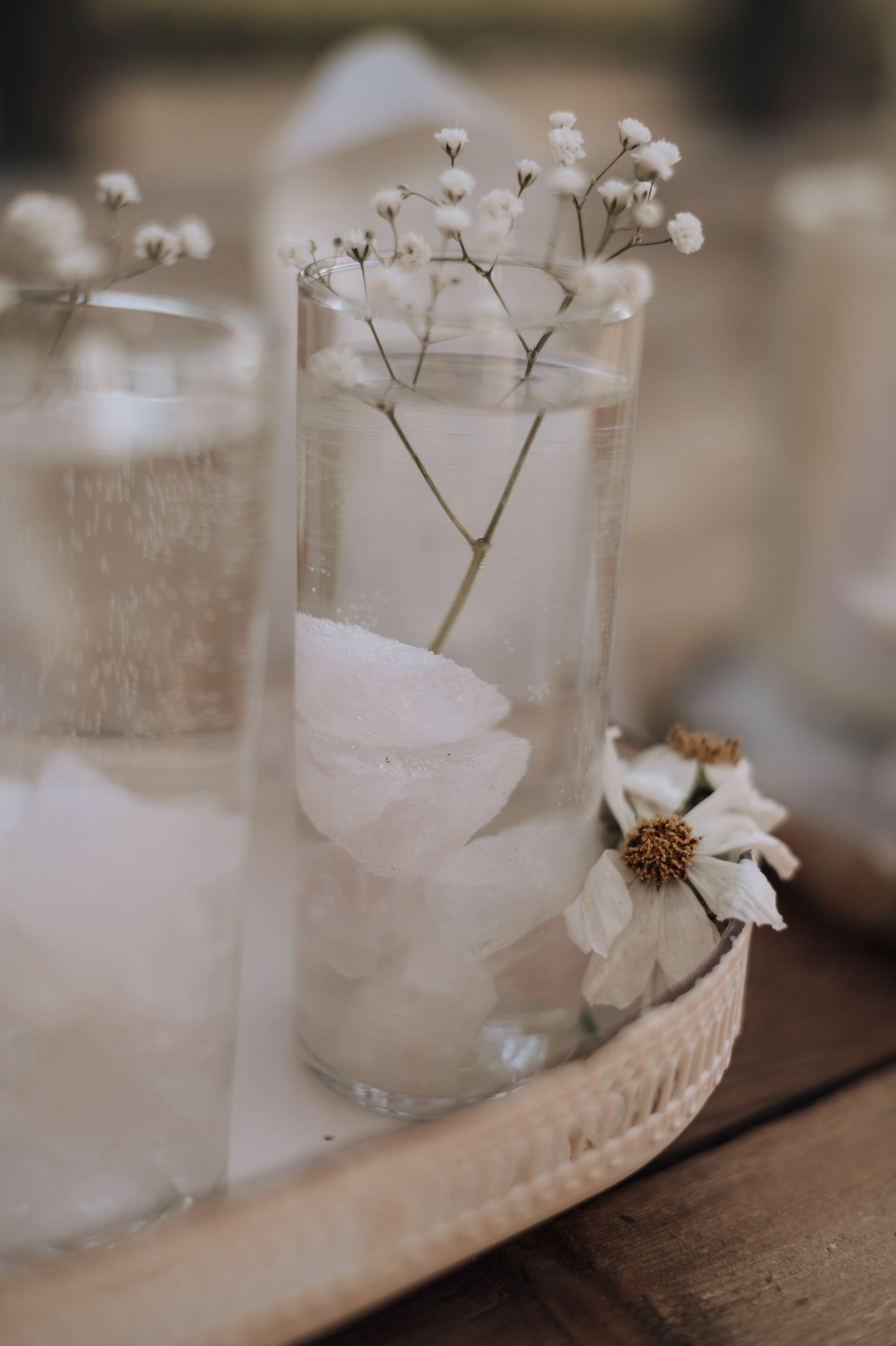 Baby's breath in clear glass vase with white floral accents on wooden surface.