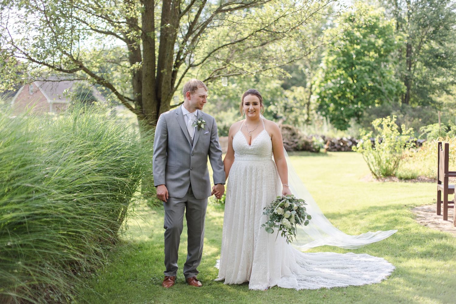 Wedding party walking through a lush green garden path on a sunny afternoon.