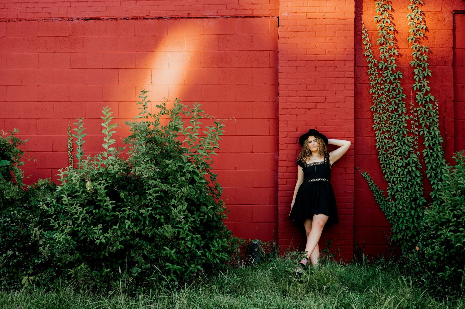 A fashion portrait against a red brick wall with climbing vines and natural lighting.