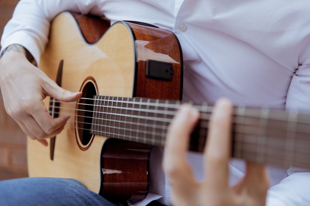 Close-up of hands playing acoustic guitar strings in natural lighting.