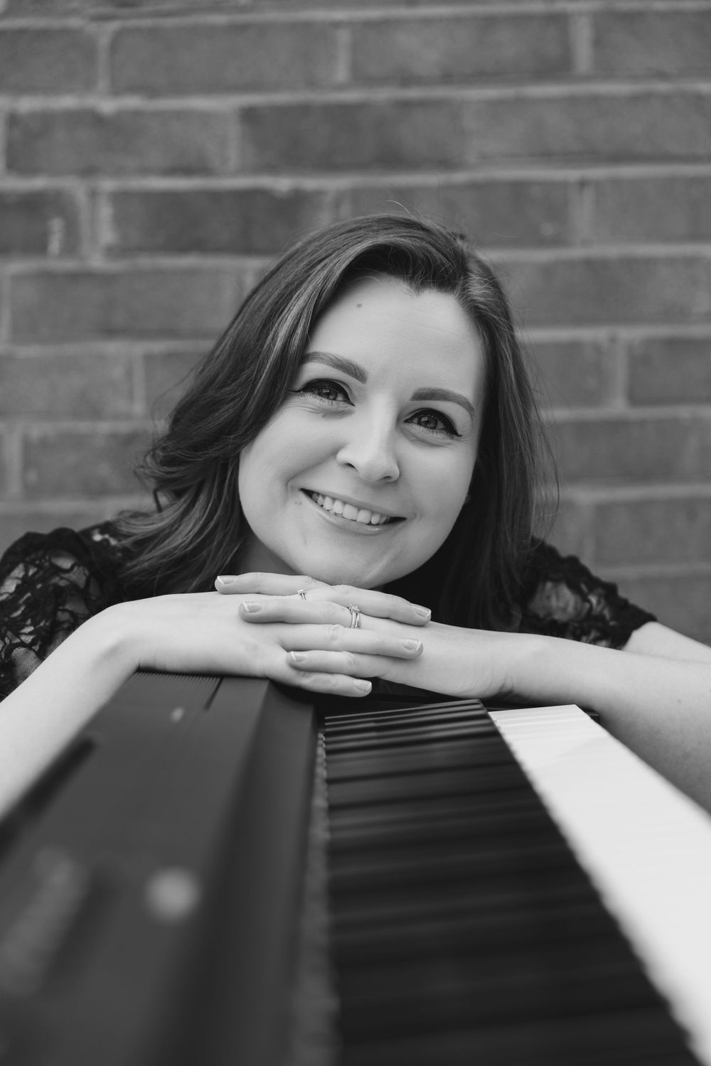 Black and white portrait of person resting on piano keys with gentle smile.