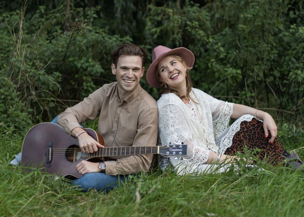 Couple sitting in grass with acoustic guitar during outdoor photo session.