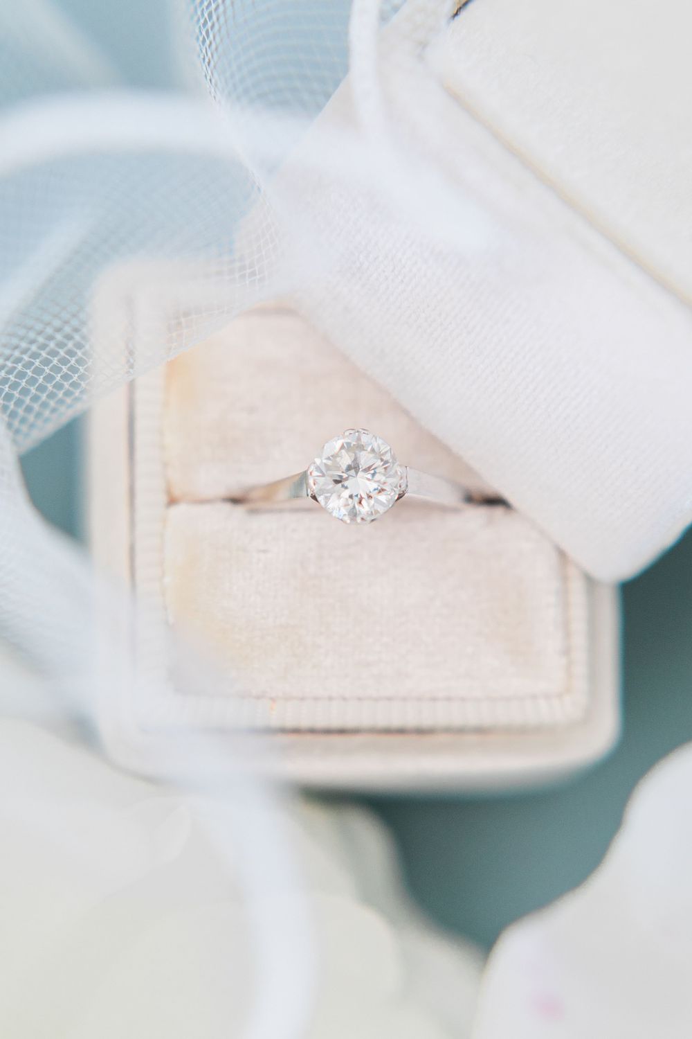 A sparkling diamond engagement ring set in a cream velvet box with delicate tulle fabric.