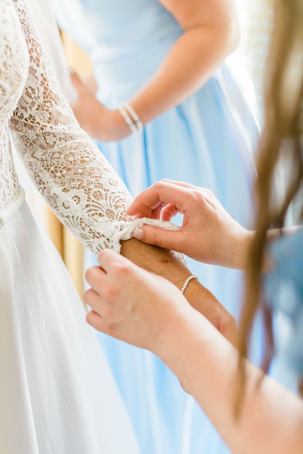 Close-up detail of delicate lace wedding dress sleeve being fastened.