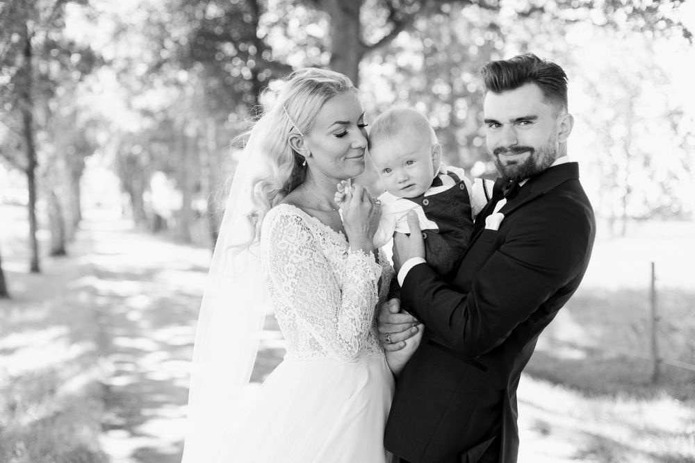 Black and white wedding photo of couple with baby outdoors.