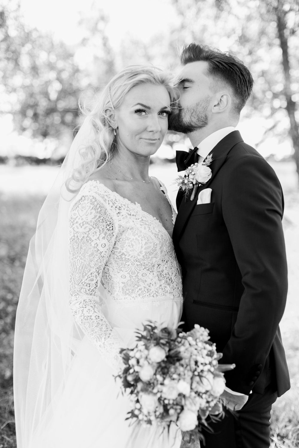 Intimate black and white portrait of newlyweds with bouquet outdoors.