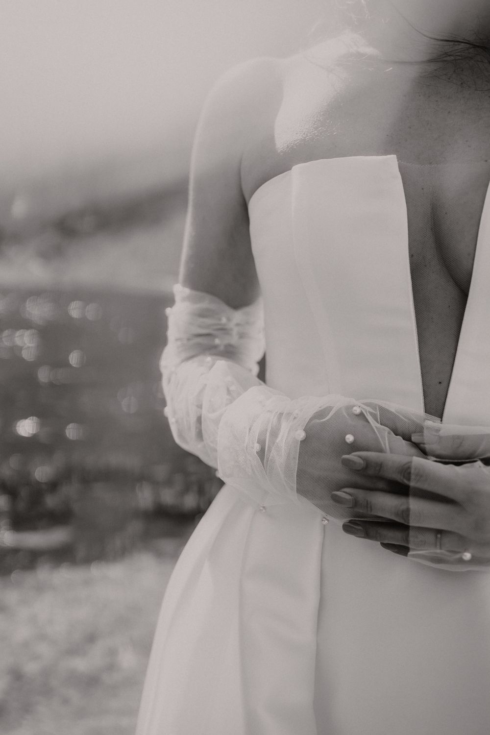 An elegant black and white detail shot of a bride's wedding dress and hands.