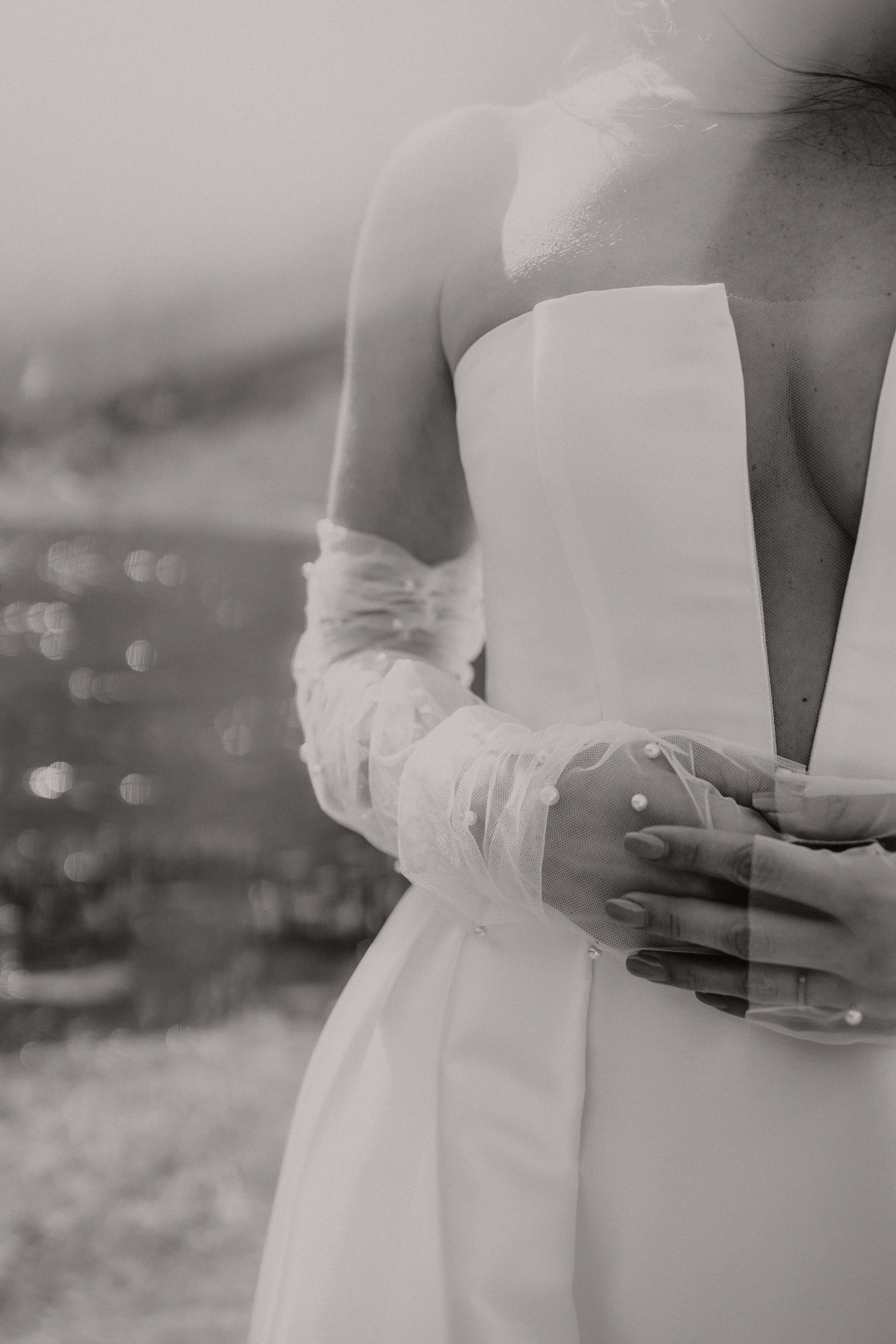 An elegant black and white detail shot of a bride's wedding dress and hands.