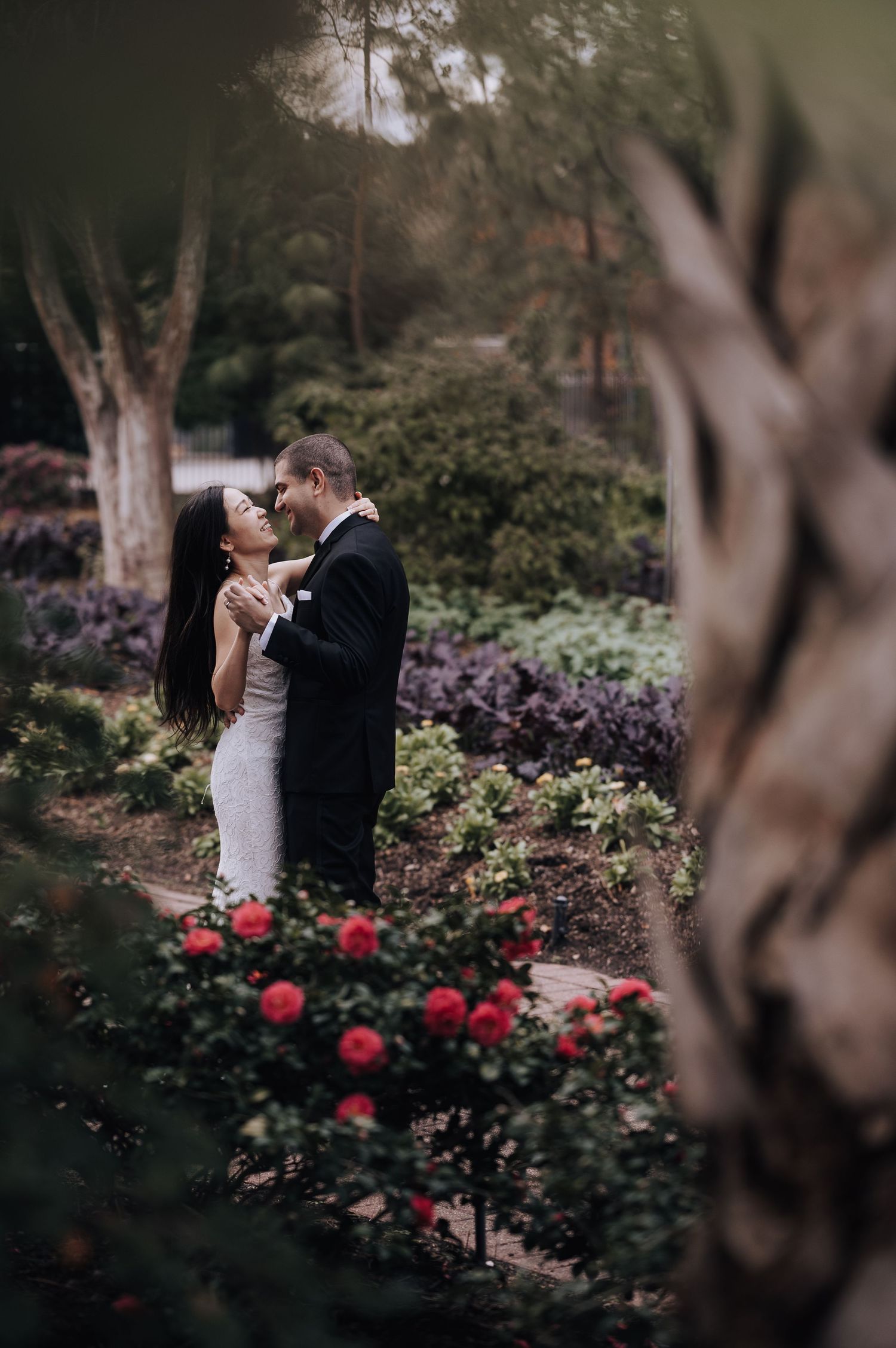 An intimate wedding moment captured in a garden with blooming red roses and natural foliage.