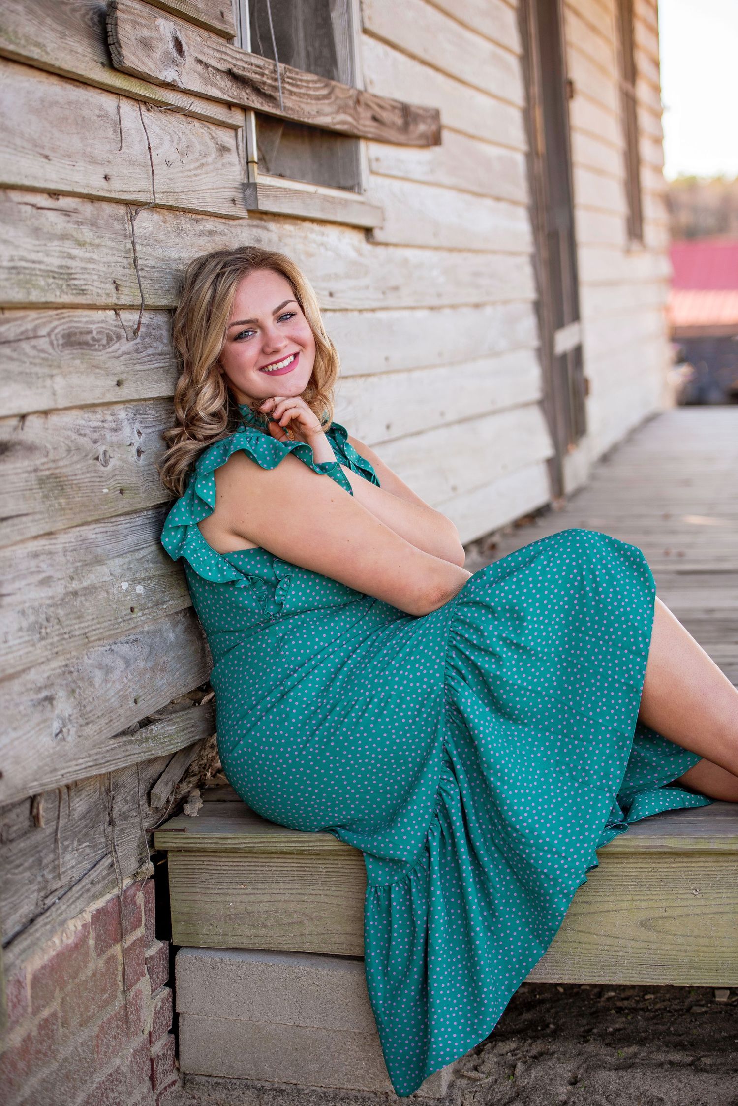 A portrait against a rustic wooden wall wearing a teal polka dot dress.