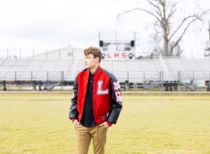 senior boy in letterman jacket on school football field