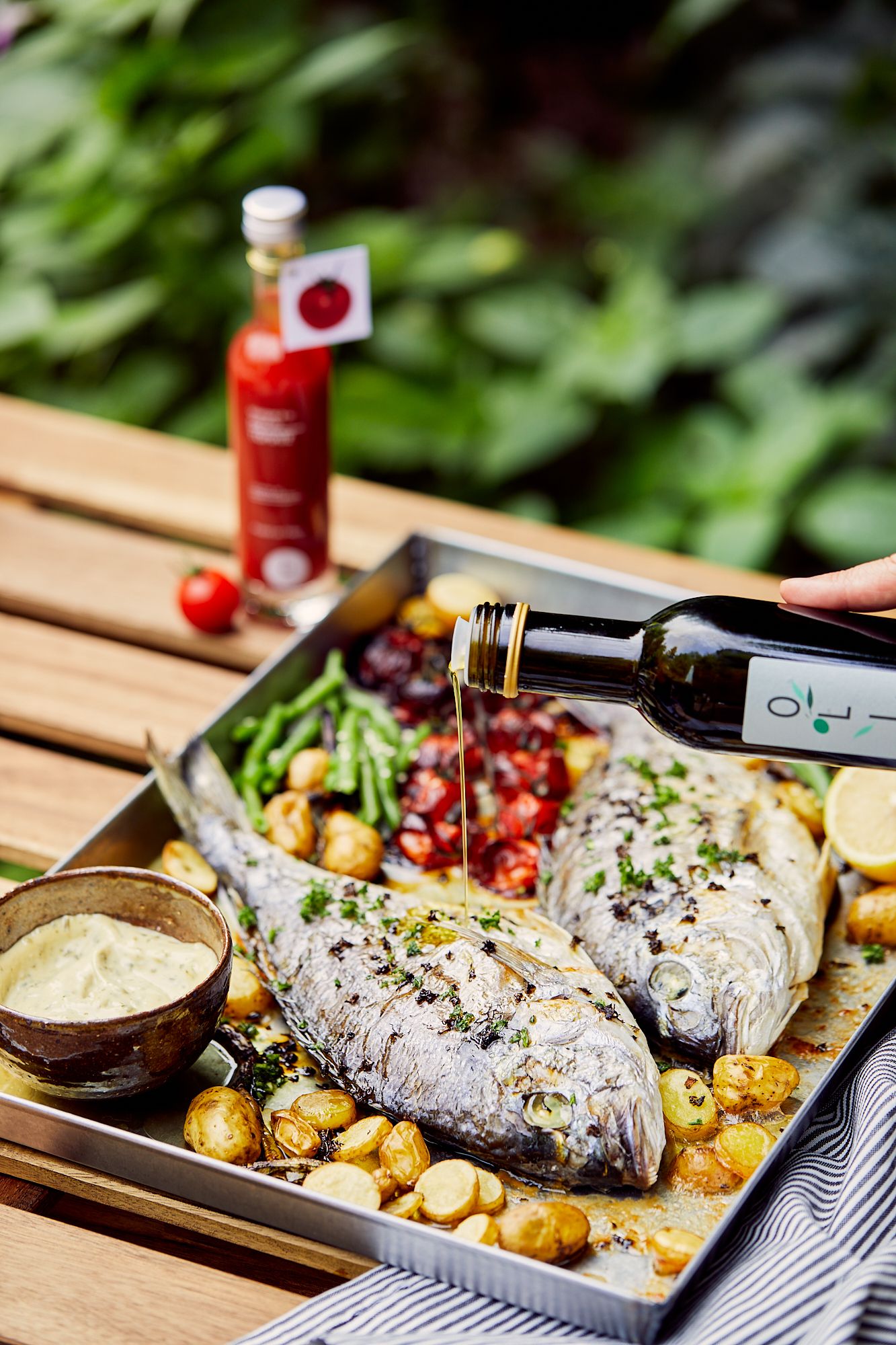 Grilled fish served with roasted potatoes and grapes on a wooden outdoor table.