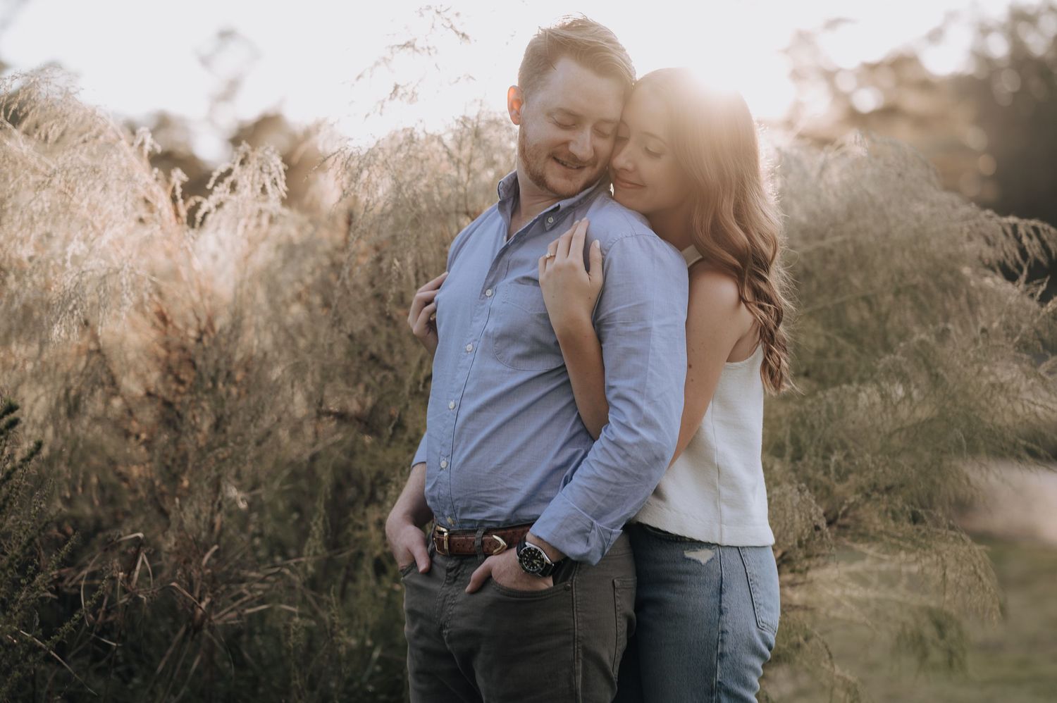 A couple shares an intimate moment in a sunlit field of tall grass.