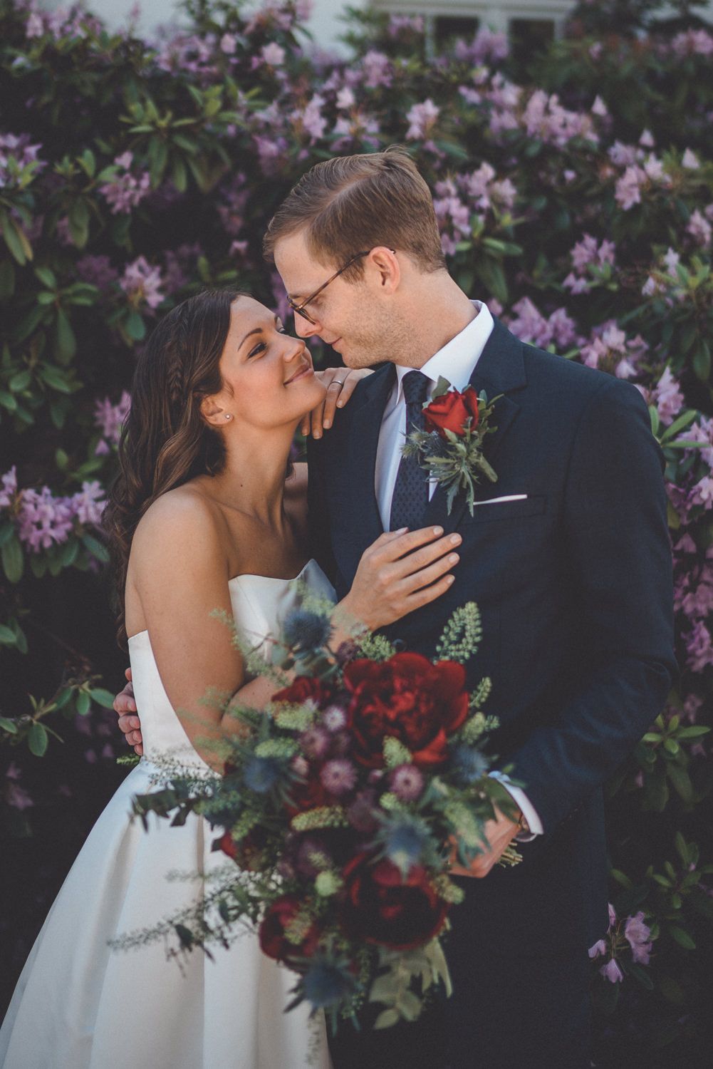 Brudpar tittar på varandra och ler före sin ceremoni i Stockholm framför blommande rhododendron