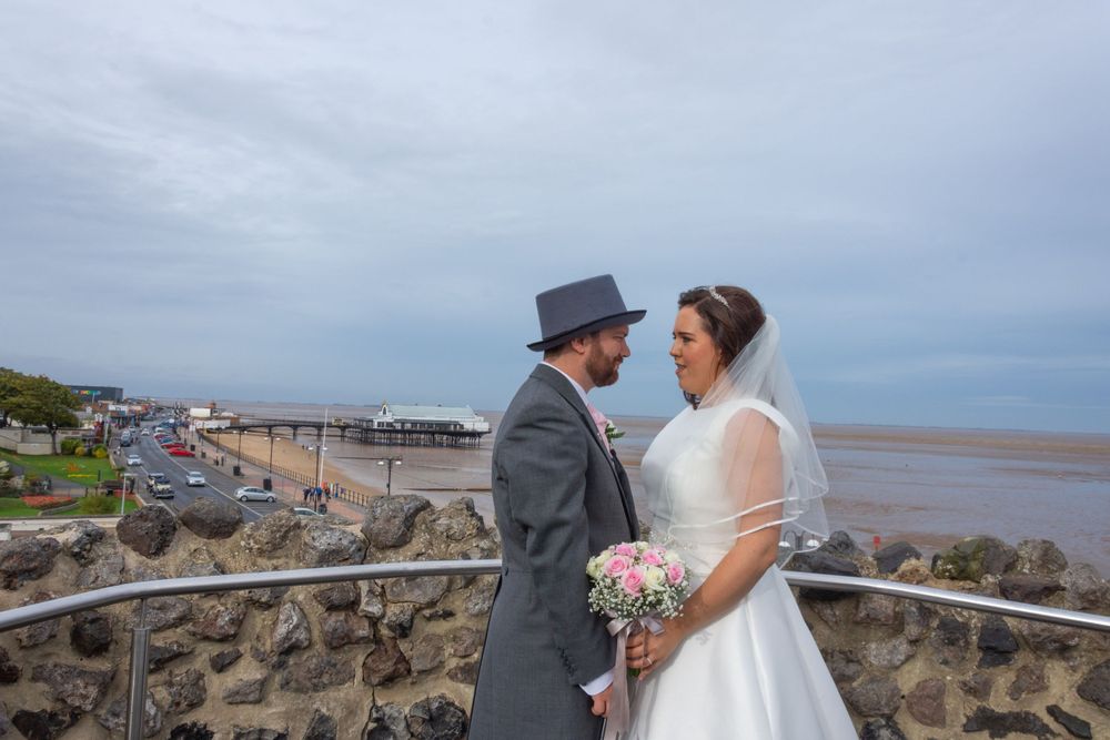 Coastal wedding portrait with dramatic cloudy sky and beach backdrop.