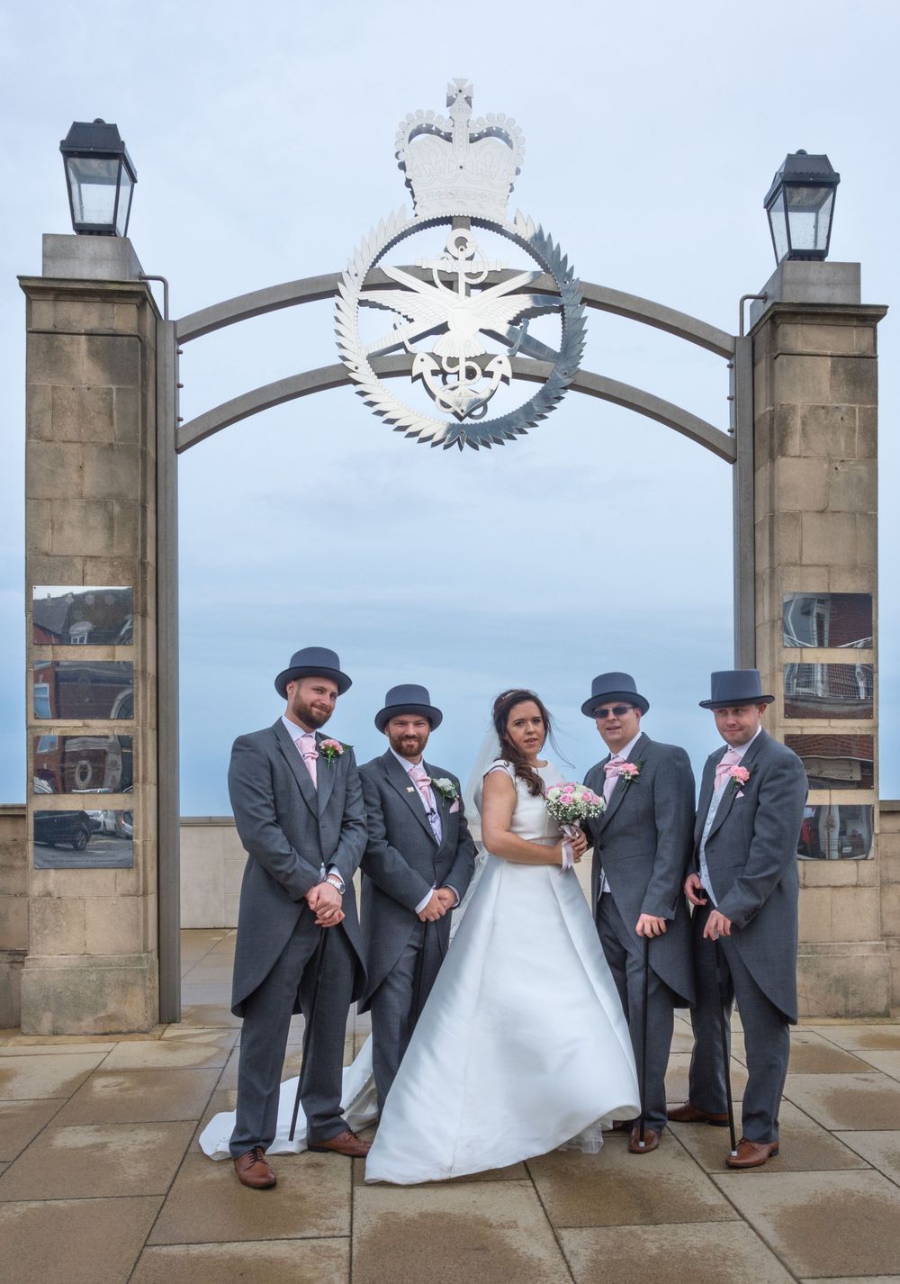 Wedding party poses beneath an ornate archway with lanterns and decorative metalwork.
