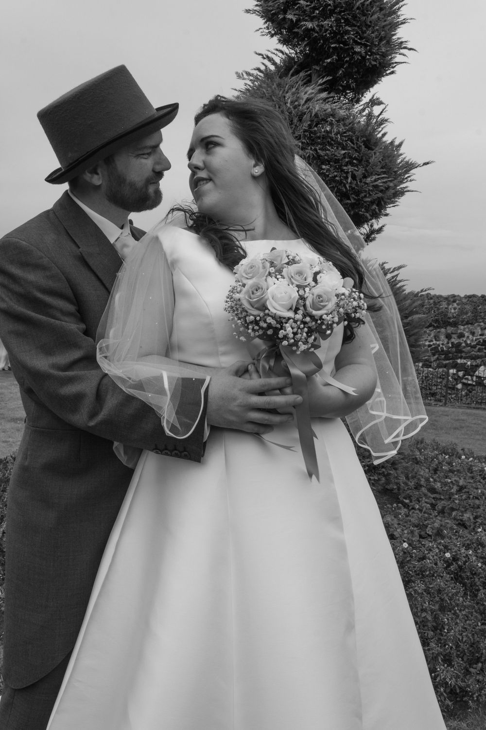 Black and white portrait of couple in vintage wedding attire with bouquet outdoors.