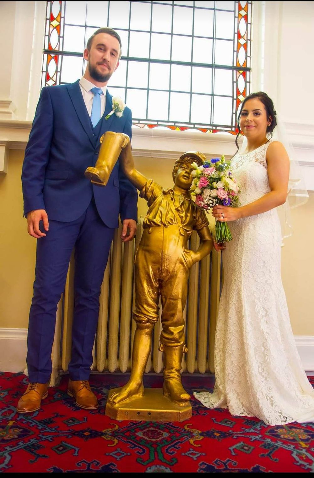 Wedding couple posing with golden statue in front of stained glass window.