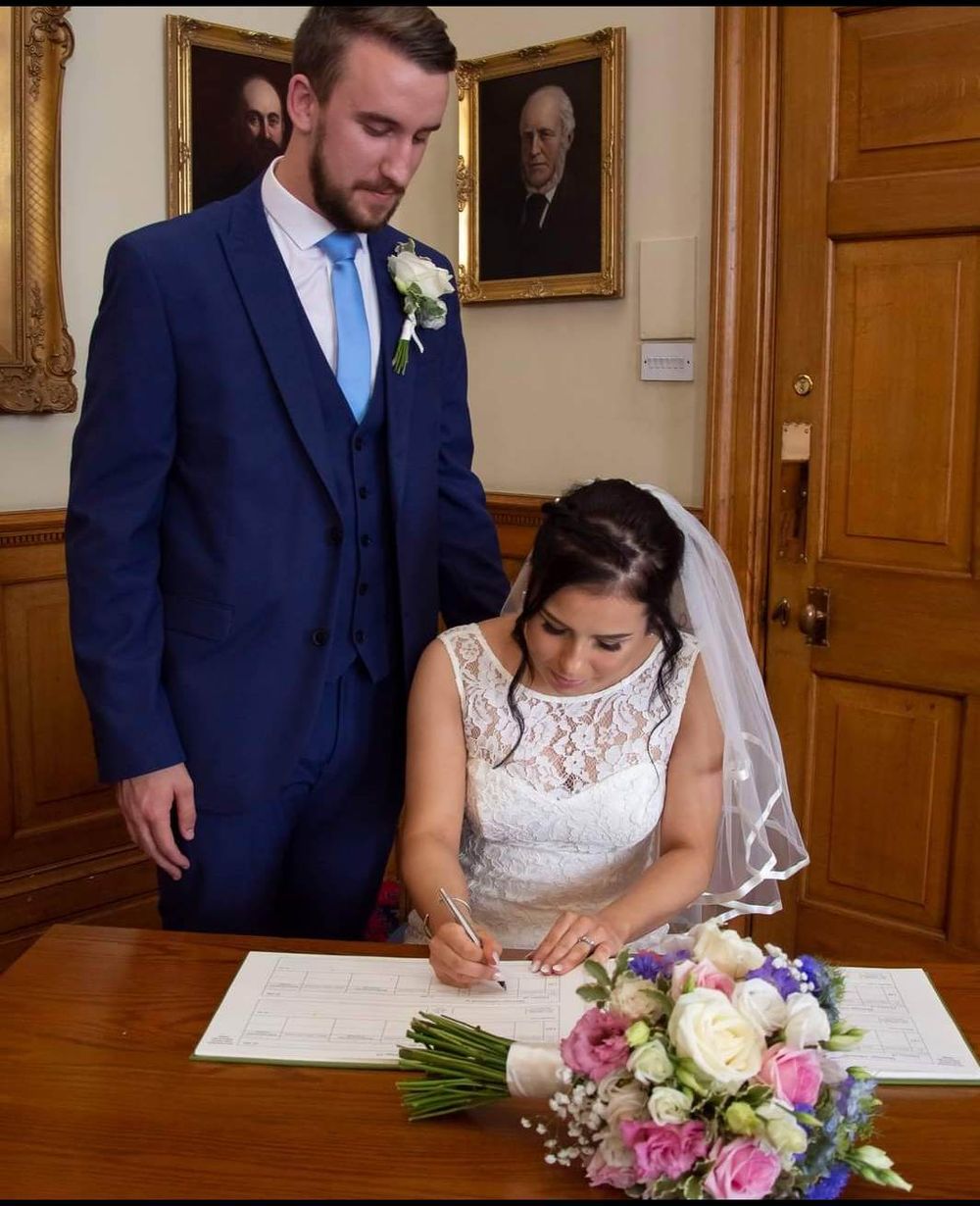 Wedding ceremony signing moment with bridal bouquet of pink and white flowers on wooden table.