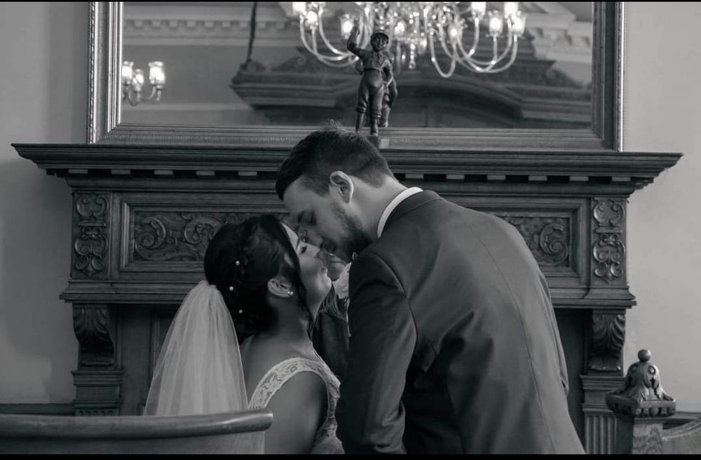 Black and white wedding moment captured in front of ornate fireplace mantle.