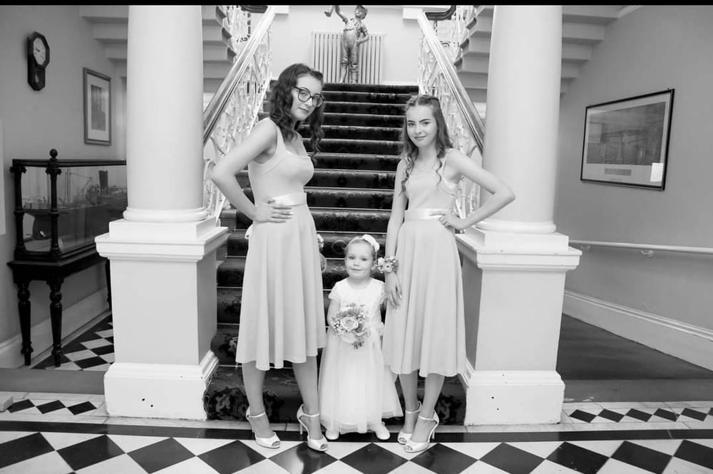 Black and white photo of three people in formal attire standing by grand staircase.