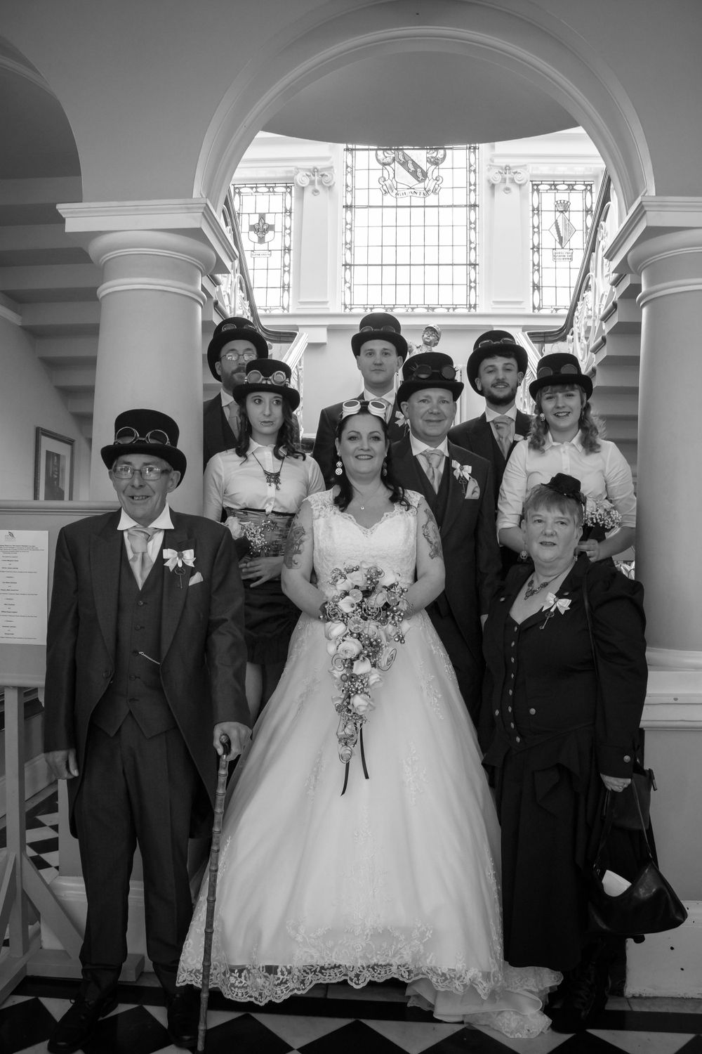 Formal black and white wedding party portrait under elegant architectural arches.
