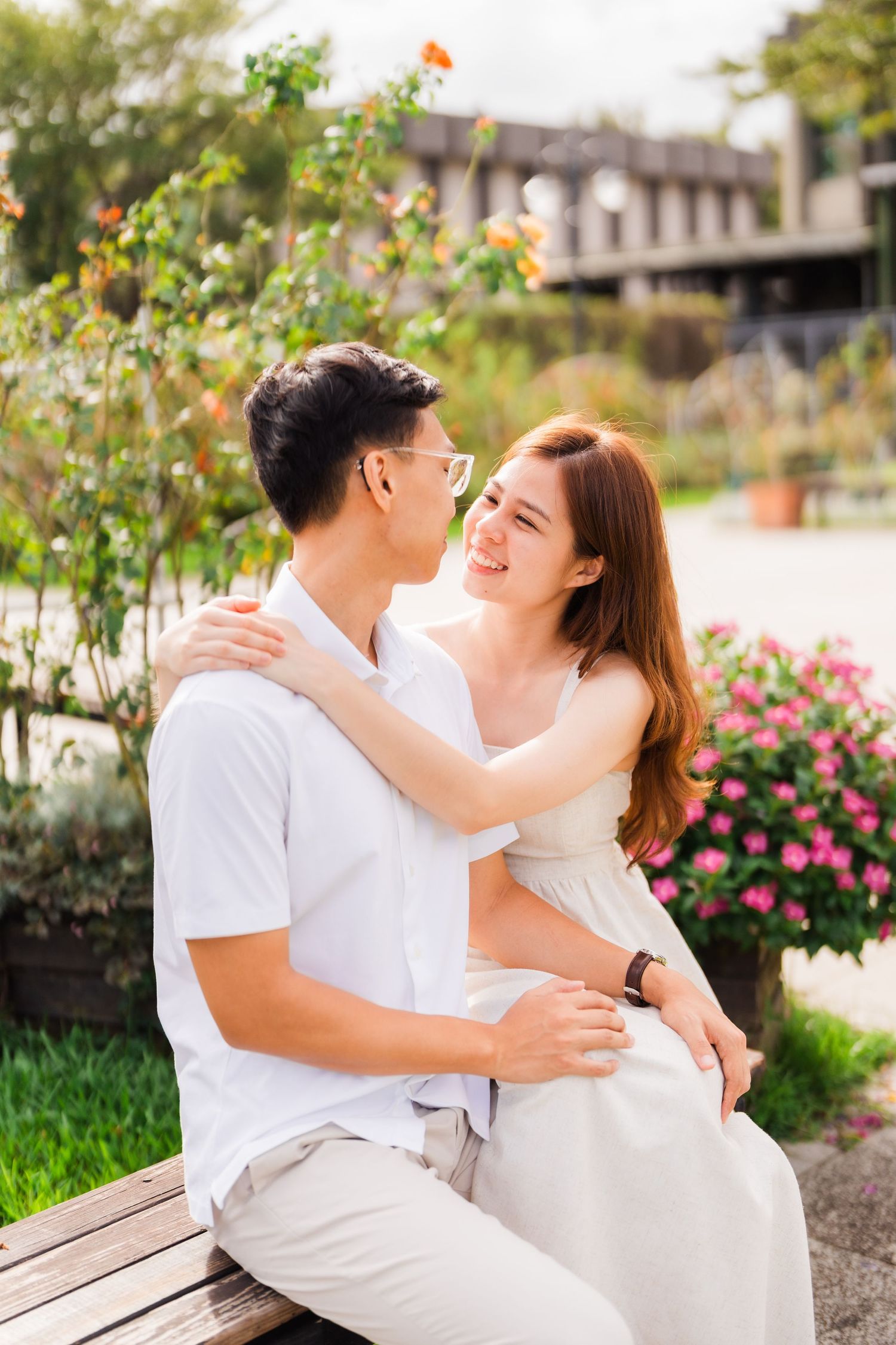 A joyful couple embraces on a bench in a vibrant garden filled with colorful flowers.