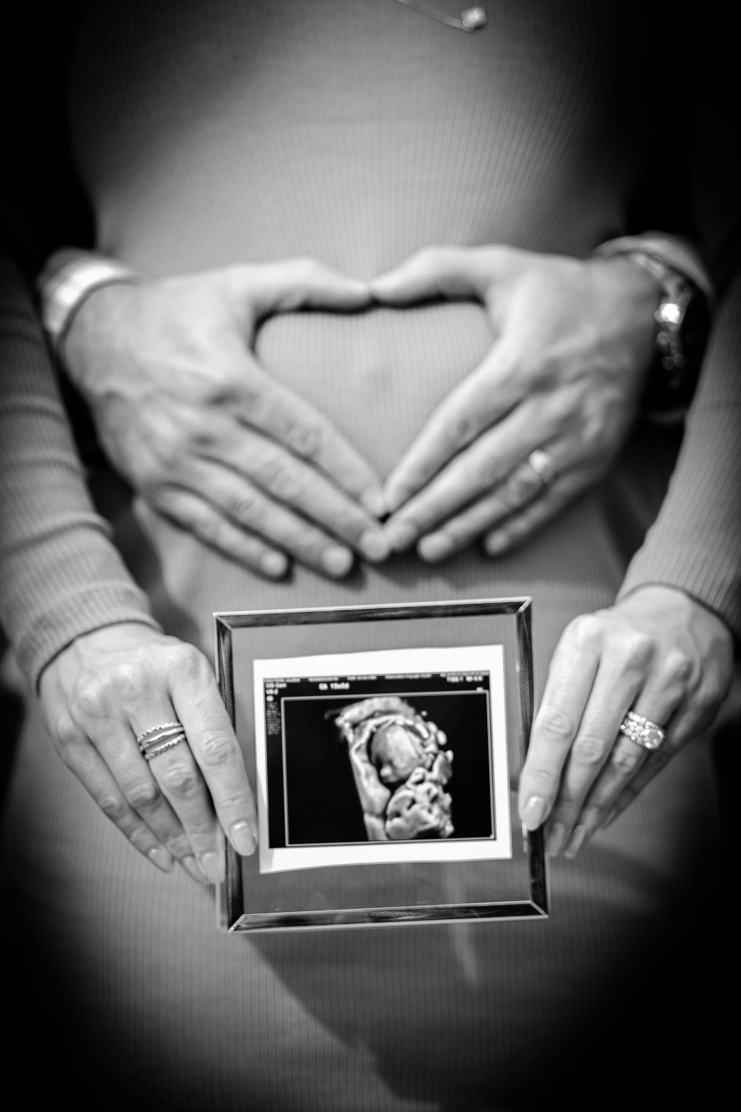 A sonogram is focused in the foreground while the husband creates a heart around his wife's protruding belly