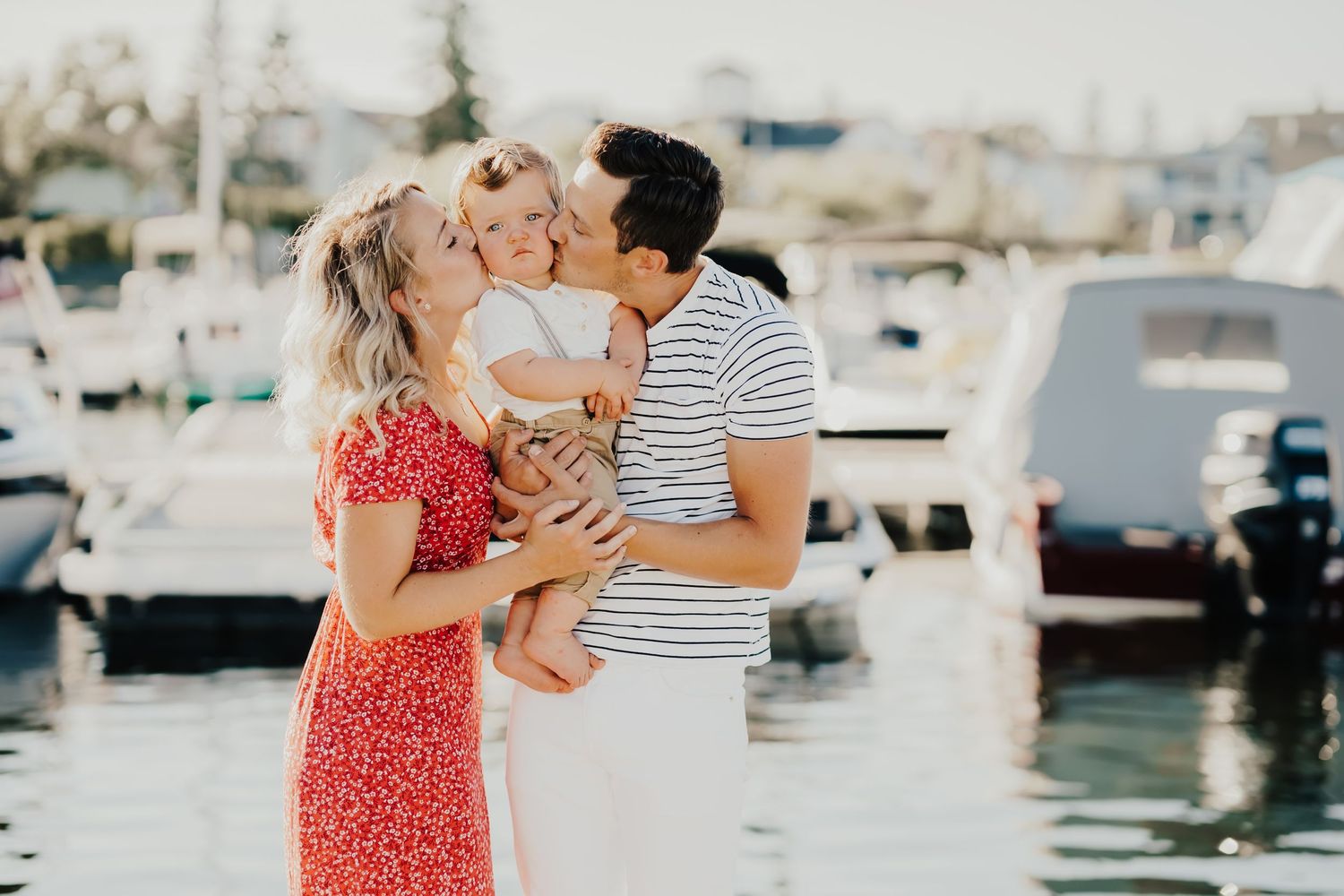 Couple embracing near boats at a sunny marina with sparkling water in the background.