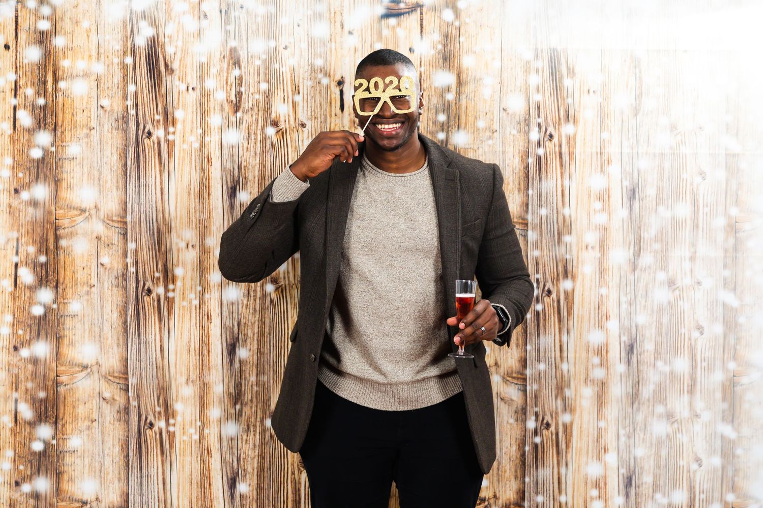 Man in blazer holding champagne wearing 2021 novelty glasses at New Year celebration.
