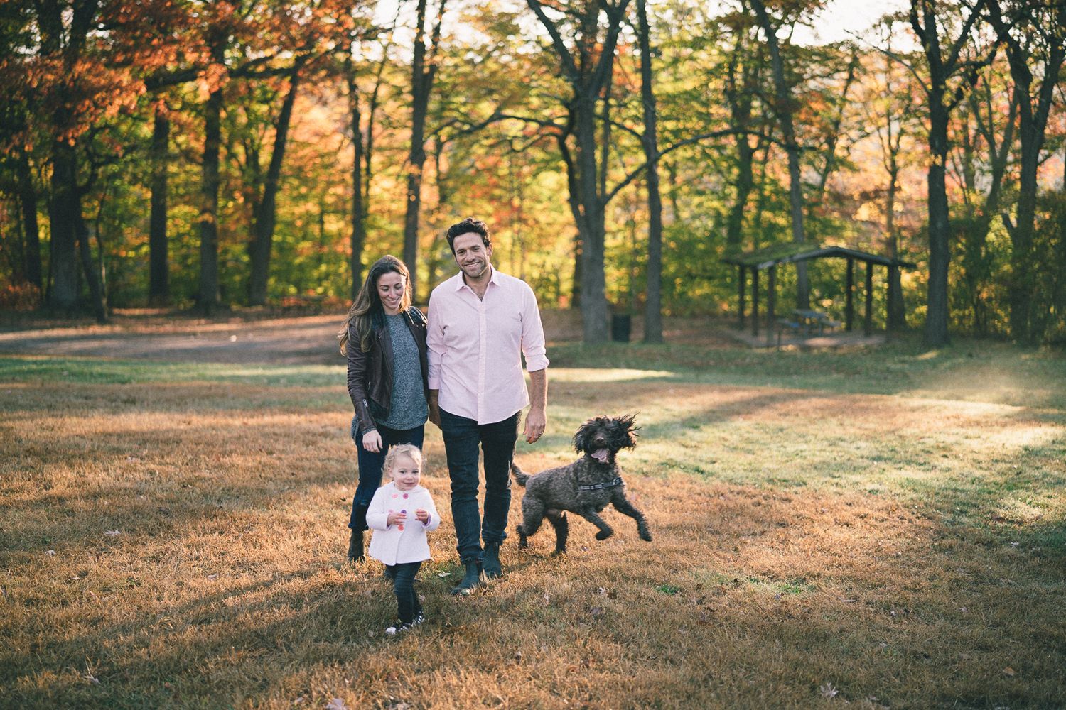 Family and their dog enjoying an autumn walk in a park with golden sunlight.