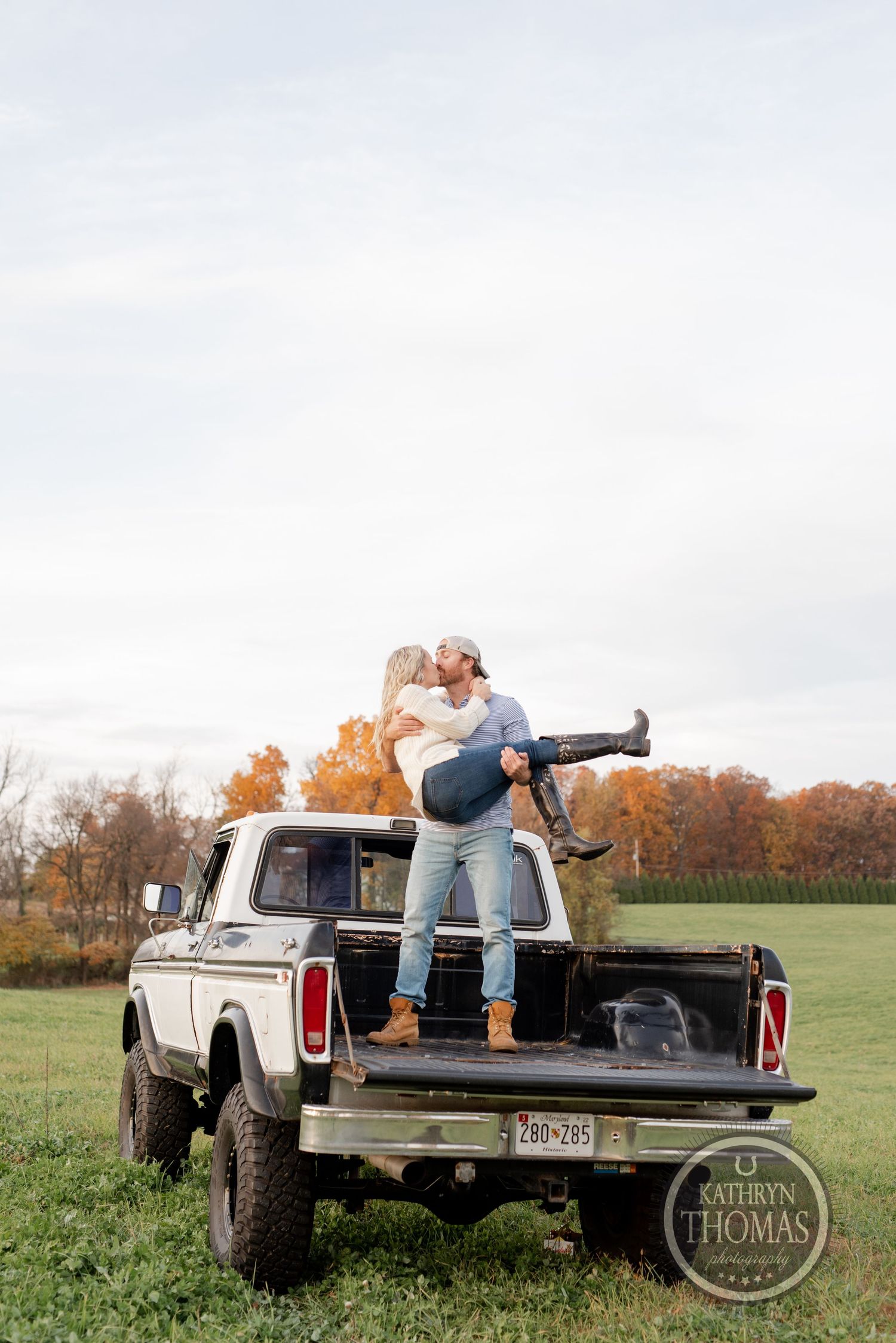 Couple sitting on vintage Ford truck bed against autumn sky and fall foliage.