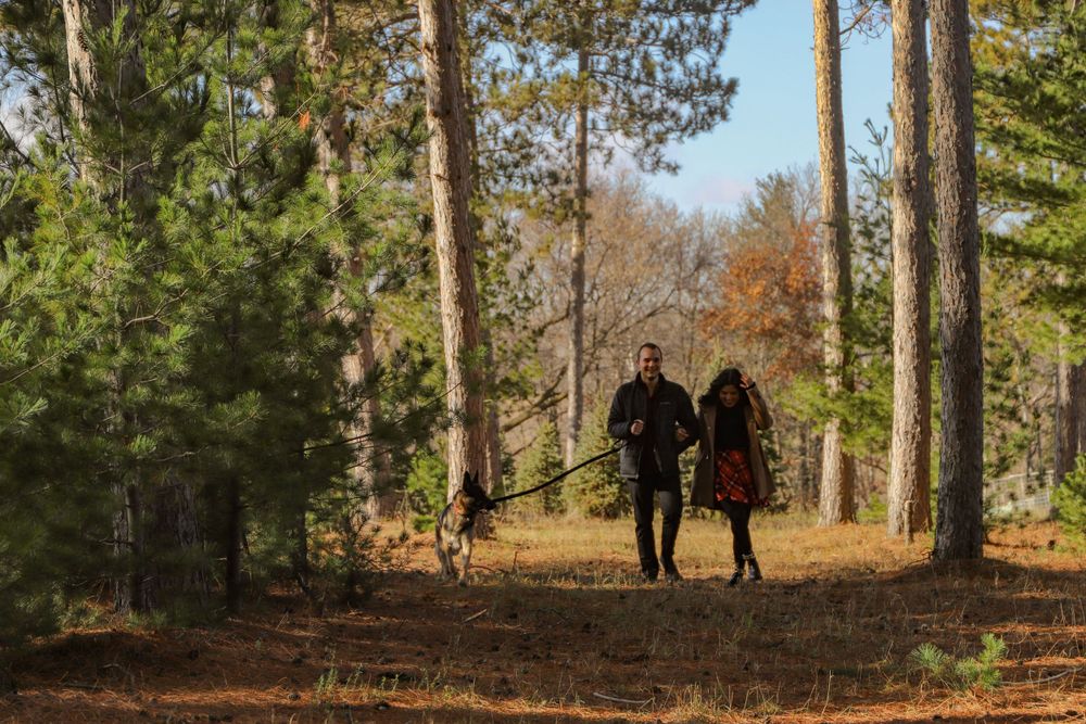 Couple walking their dog through a wooded trail during autumn.