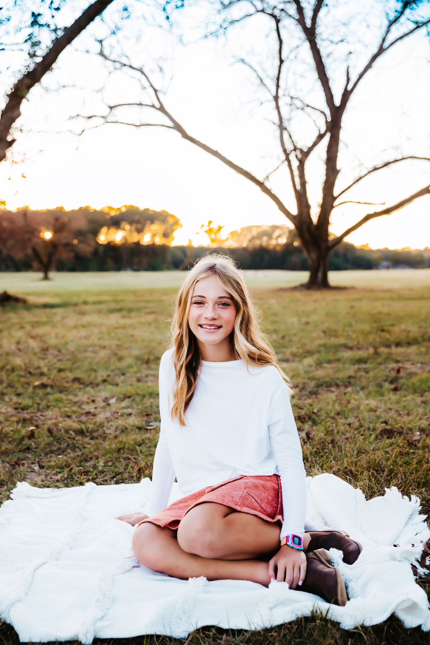 Outdoor portrait session on a white blanket during golden hour beneath a large tree.