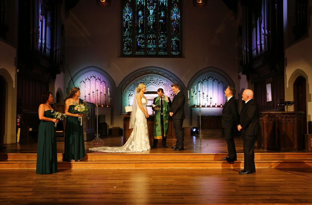 Wedding ceremony taking place in a beautiful church with stained glass windows and gothic architecture.