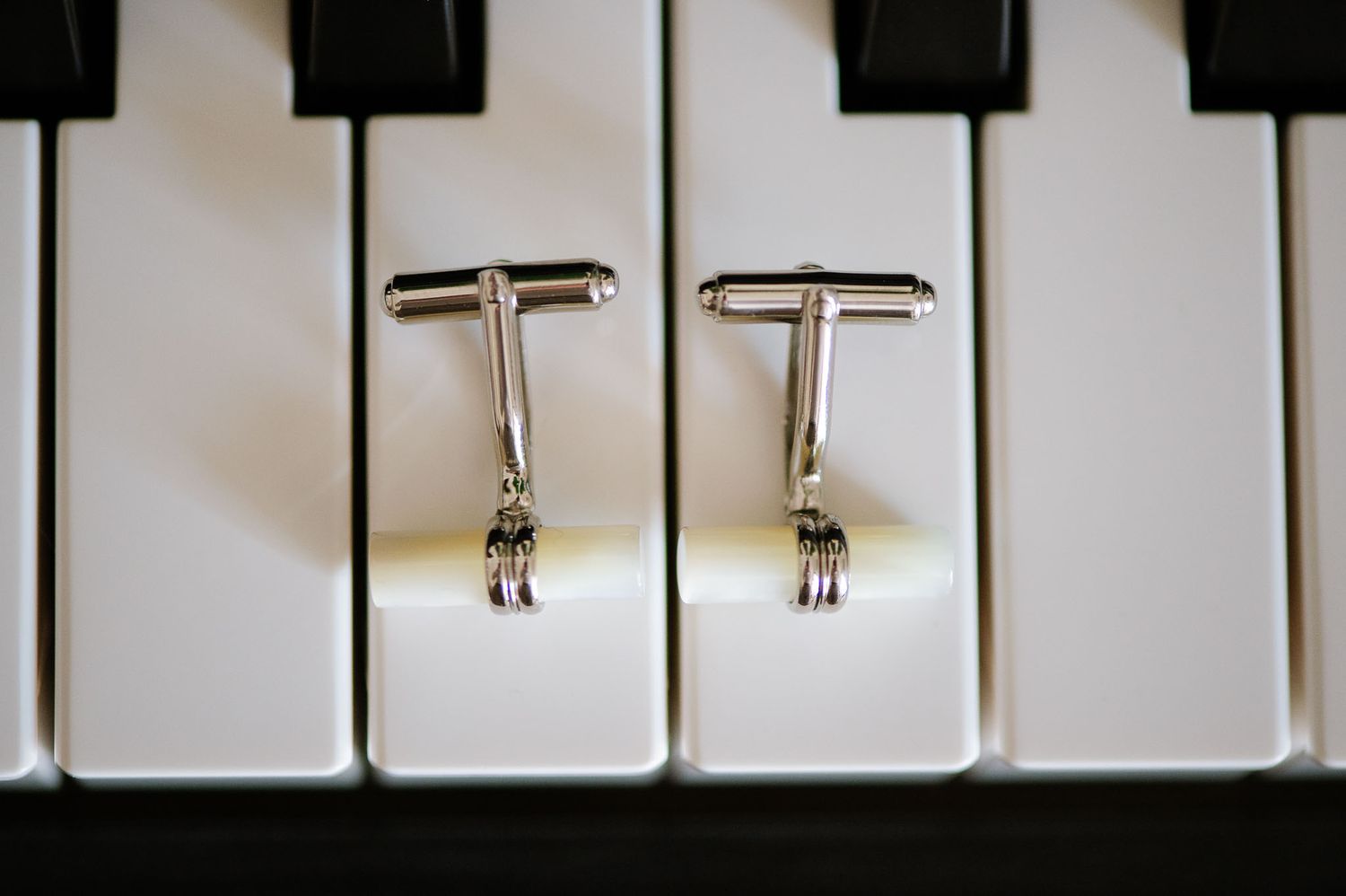 Silver cufflinks arranged on black and white piano keys.
