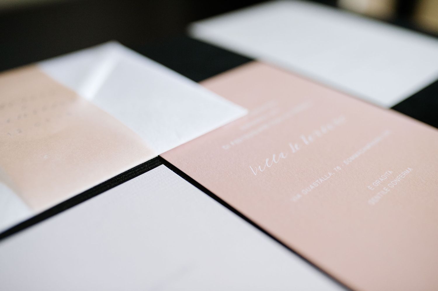 Minimalist wedding invitations in blush pink and white laid out on surface.