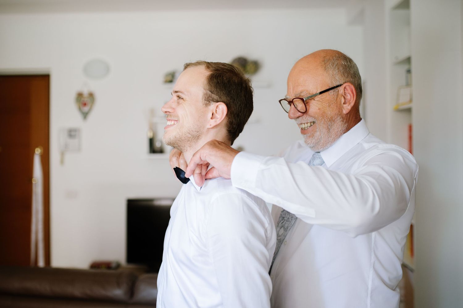Two people share a joyful moment while adjusting formal attire.