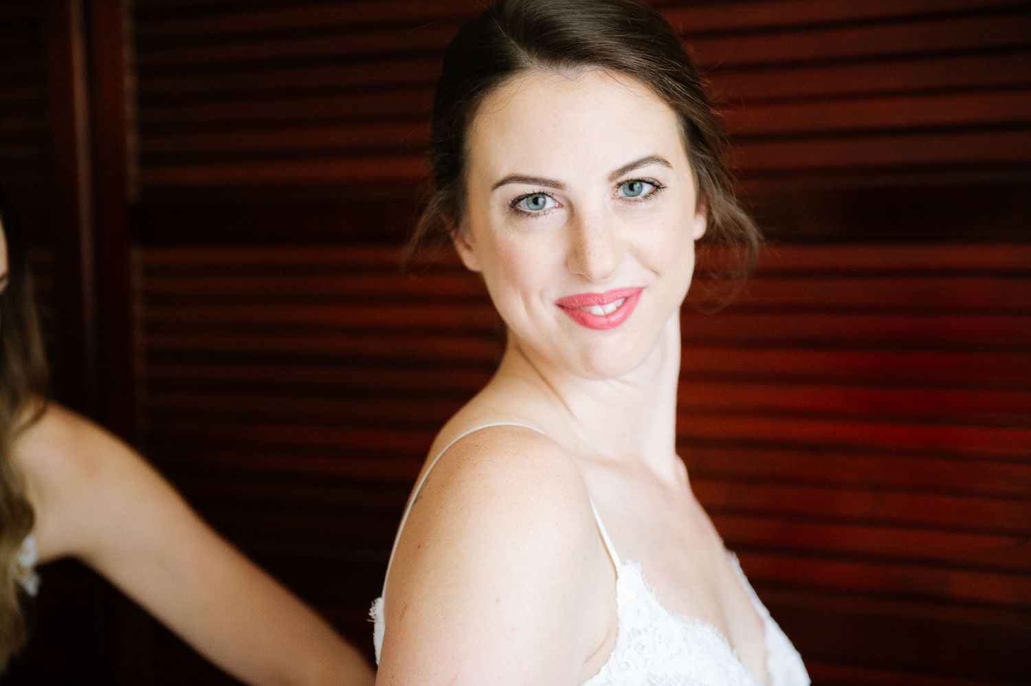 Side profile portrait against wood shutters showing bridal makeup and white dress strap.