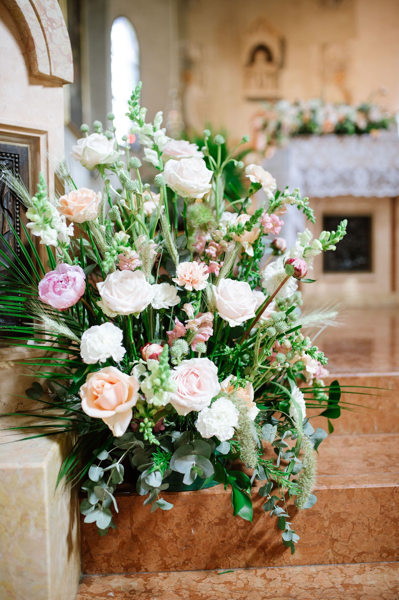 Romantic floral arrangement with pink roses and greenery decorates church steps.