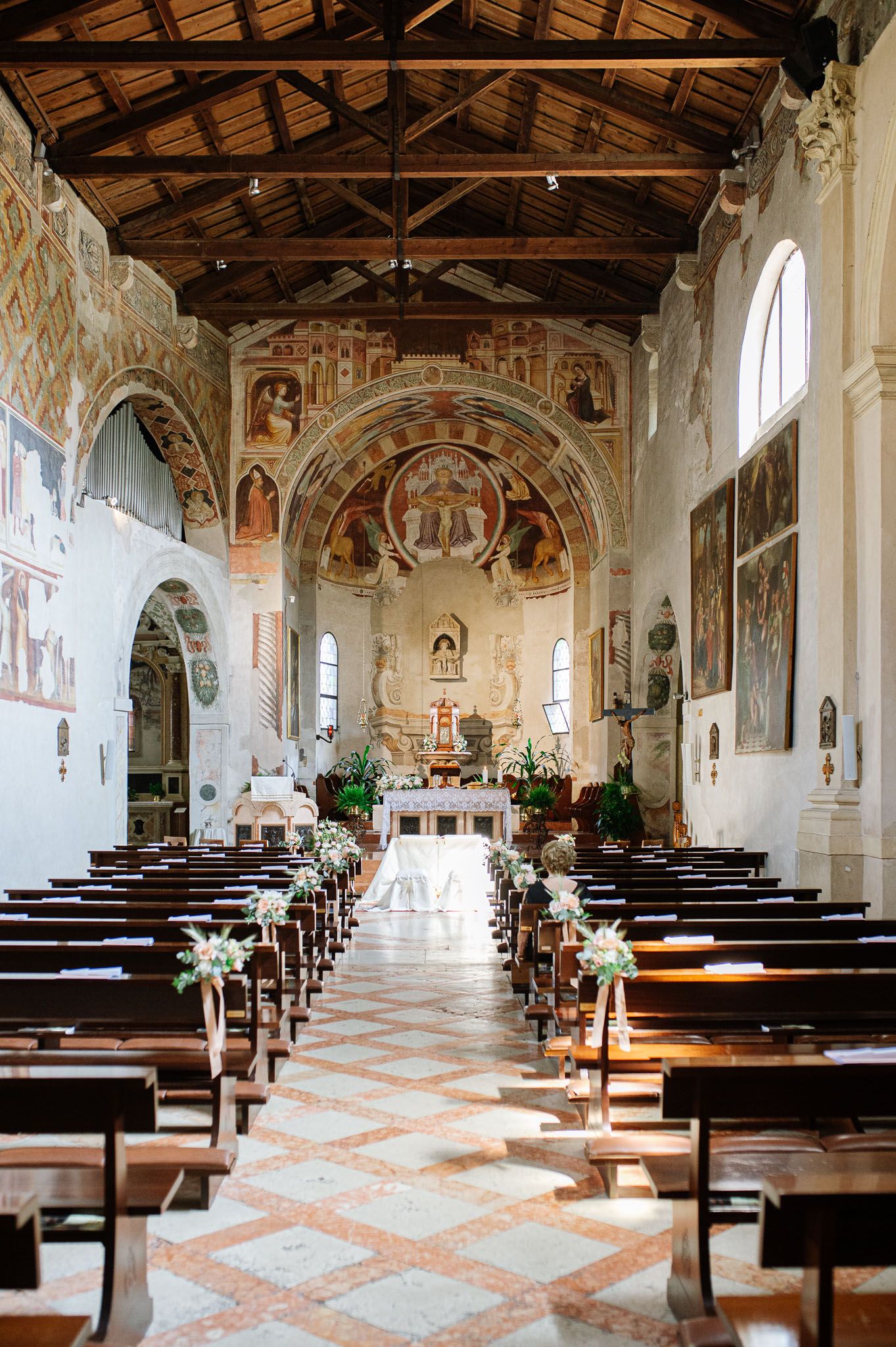 Historic church interior with frescoed walls and wooden ceiling prepared for wedding ceremony.