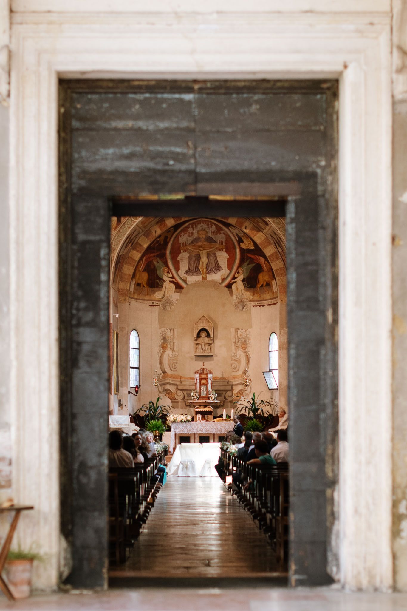 View through stone doorway into ornate church sanctuary with rows of pews and decorated altar.