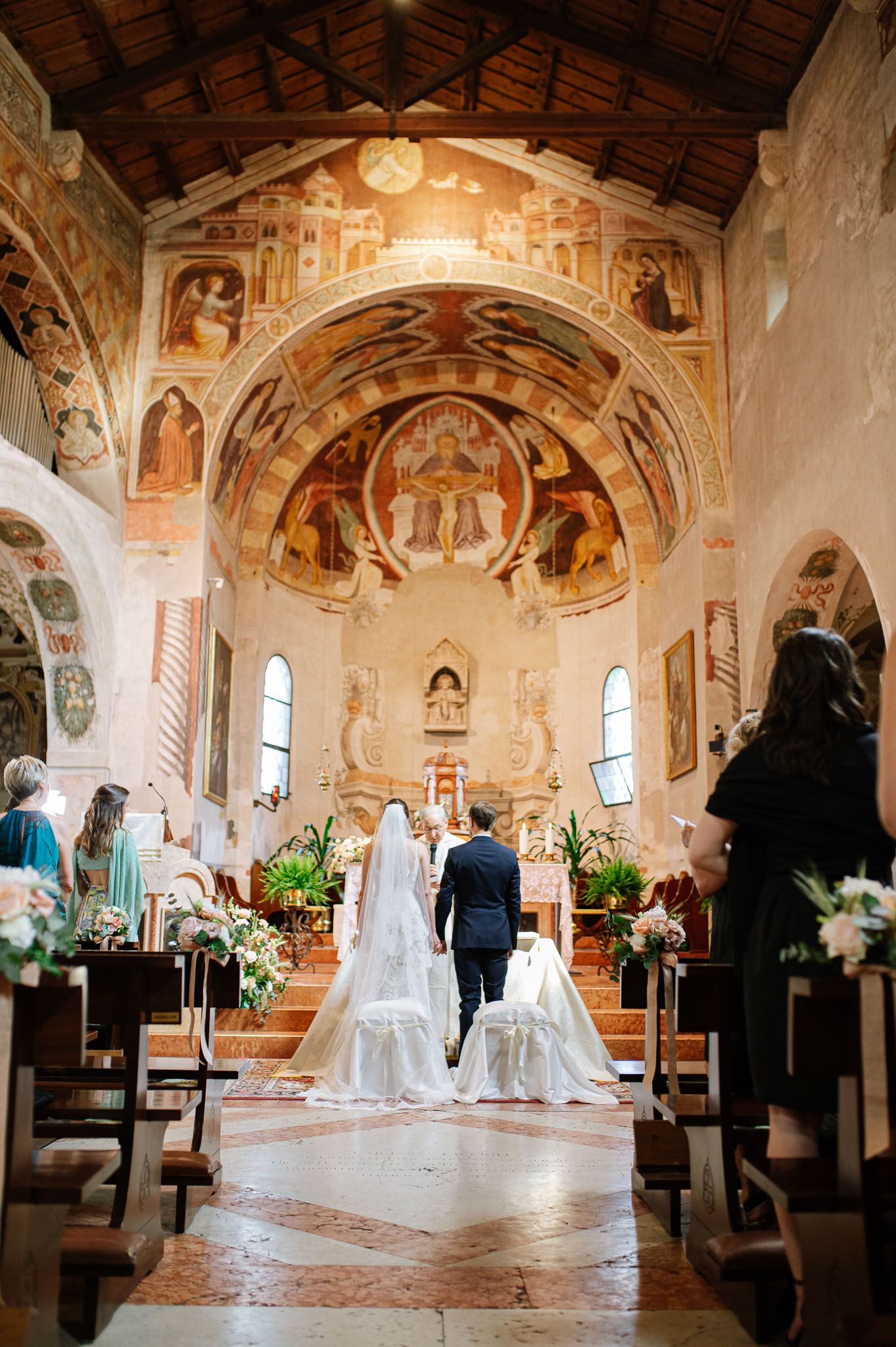 A wedding ceremony in a historic church with stunning frescoed walls and vaulted ceiling.