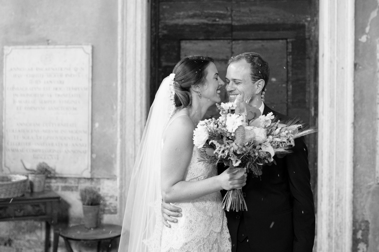 A black and white portrait of newlyweds sharing an intimate moment with bouquet.