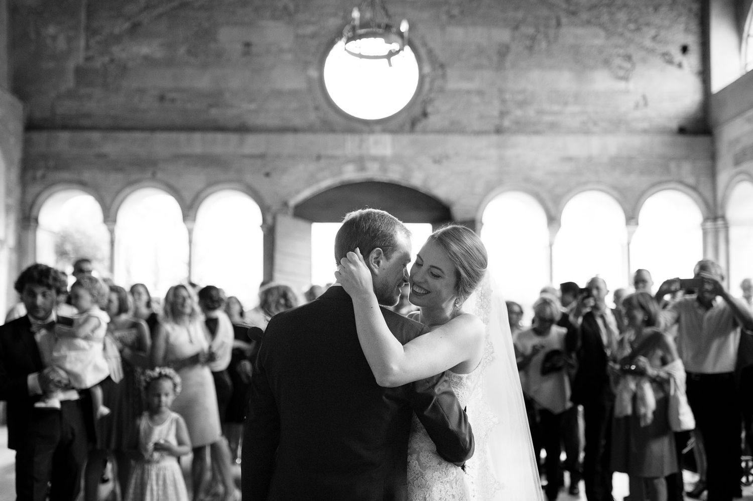 Newlyweds share their first dance surrounded by guests in a grand reception hall.