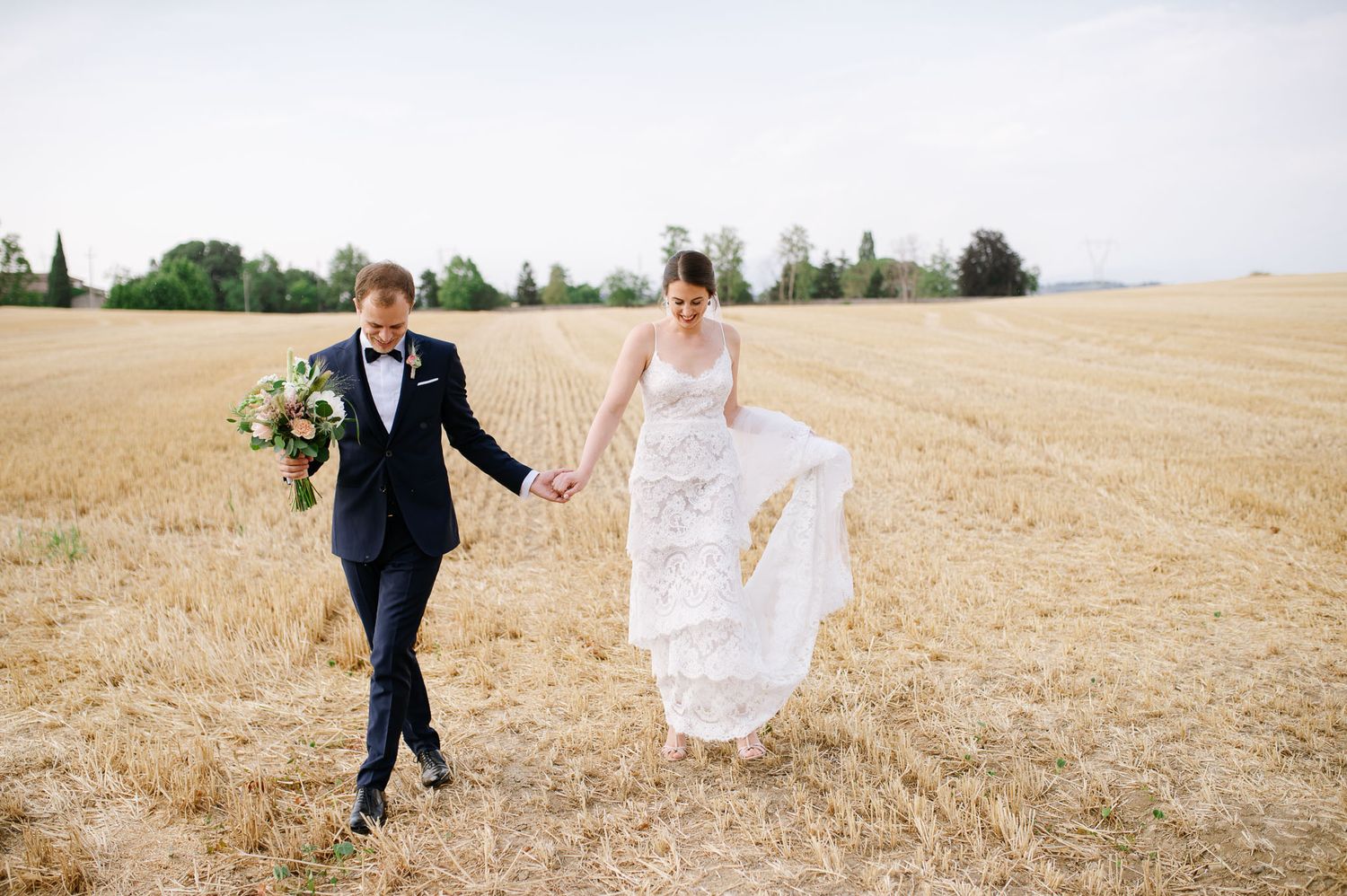 A newlywed couple walks together through a golden harvested field on their wedding day.