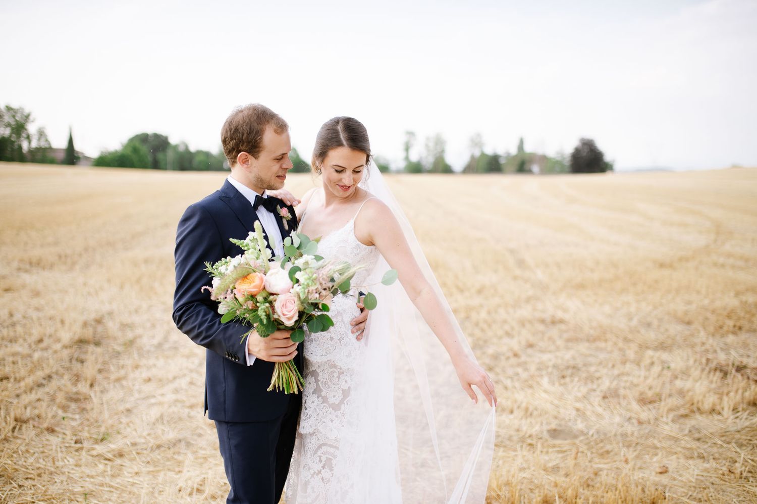 Candid wedding moment captured in a golden wheat field with flowing white veil.