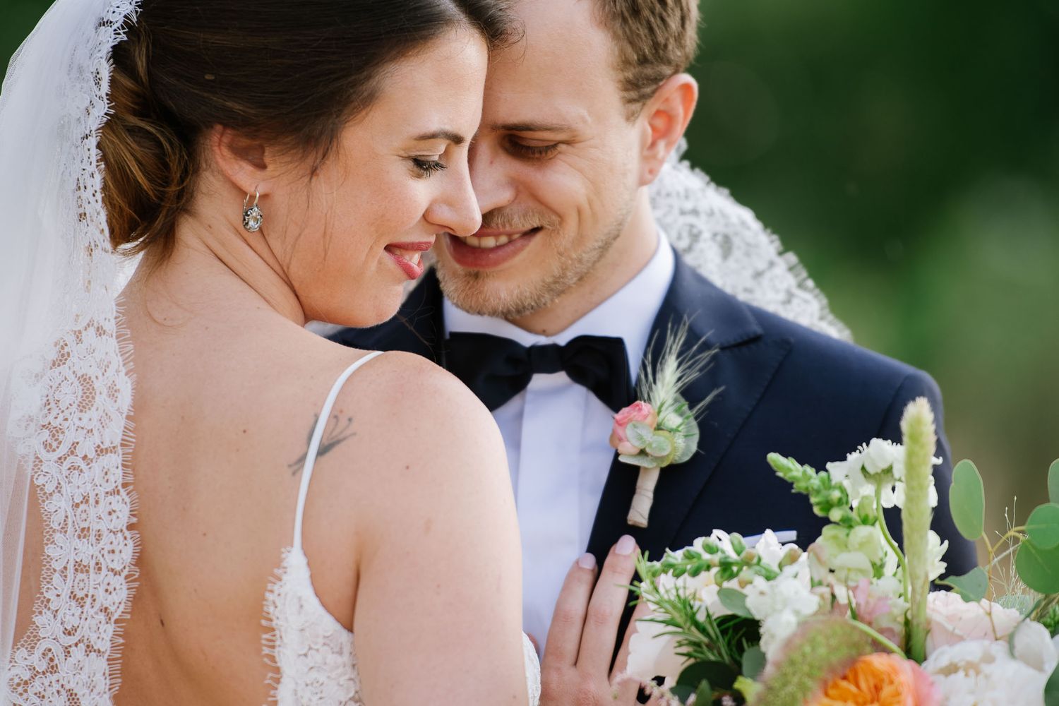 A close-up wedding portrait showing detailed lace dress and romantic embrace with spring bouquet.